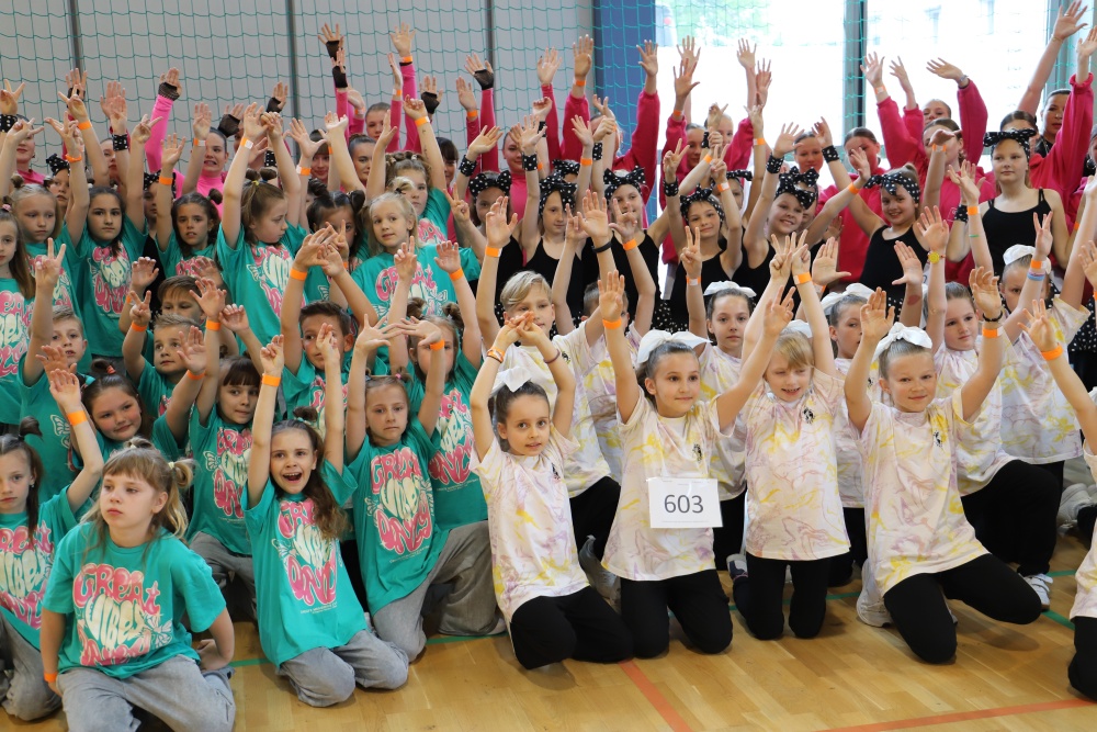 XII Ogólnopolski Turniej Tańca Nowoczesnego Taneczna Środa 2022, duża grupa młodych tancerzy z uniesionymi rękoma, maja turkusowe i białe koszulki