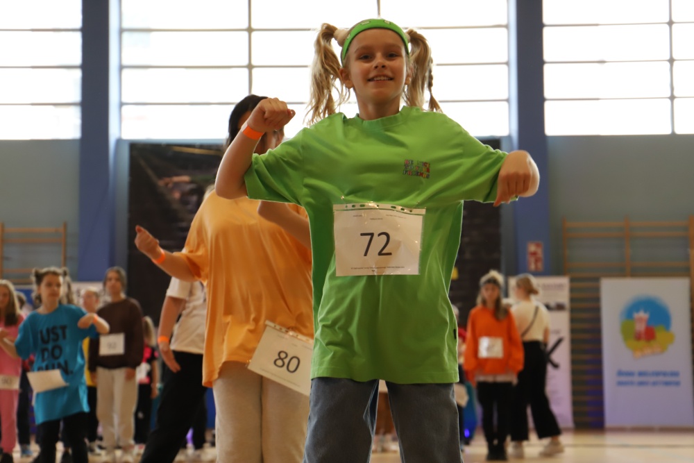 XII Ogólnopolski Turniej Tańca Nowoczesnego Taneczna Środa 2022, dziewczynka z dwiema kitkami tanczy na hali, ma zieloną koszulkę i nr 72