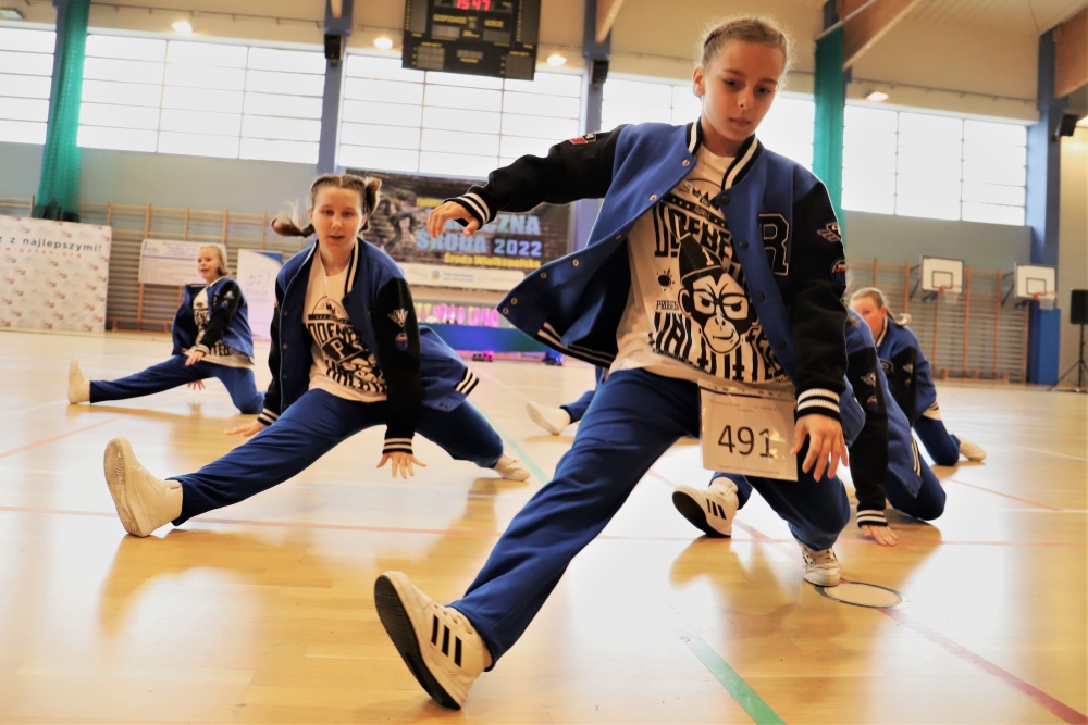XII Ogólnopolski Turniej Tańca Nowoczesnego Taneczna Środa 2022, grupa osób tańczy na hali, mają niebieskie kurki i spodnie i biało-czarne koszulki